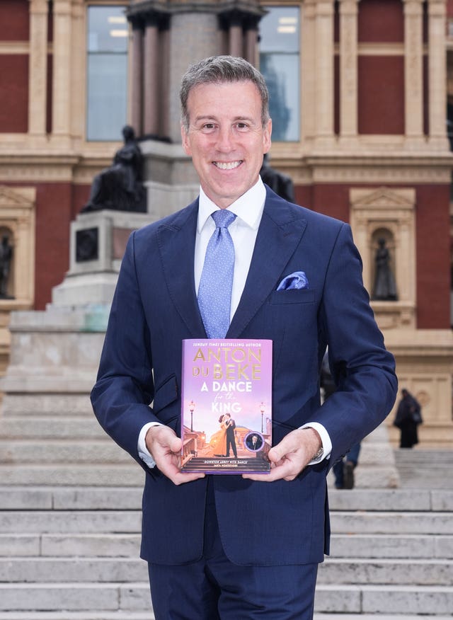 Anton Du Beke smiling while standing holding a book he wrote