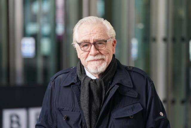 Brian Cox in a black jacket next to some glass doors