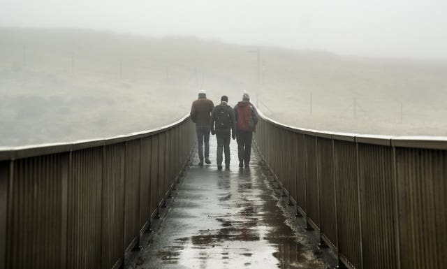 People walk over a foot bridge in foggy conditions near Saddleworth Moor