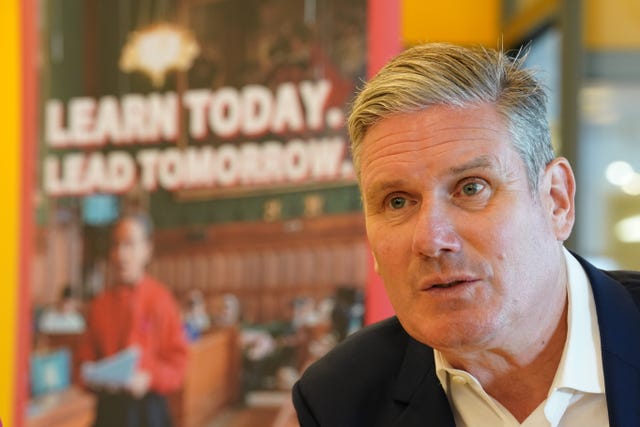 A close-up of Keir Starmer's face while visiting a school. The sign next to him reads 