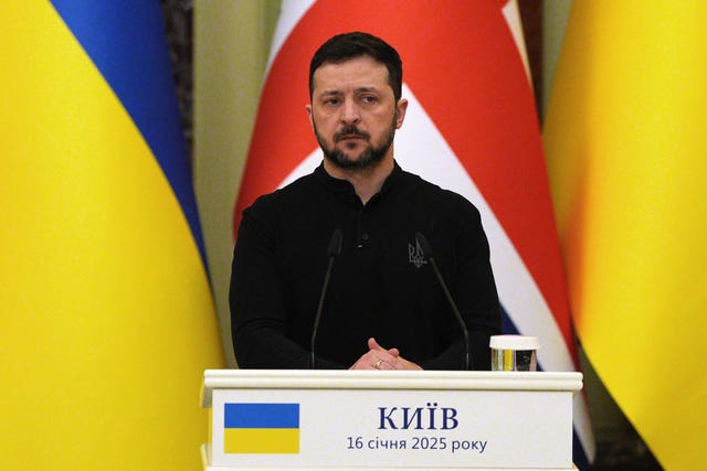 Volodymyr Zelensky stands at a lectern during a press conference in Kyiv. Ukrainian and British flags hang behind him.