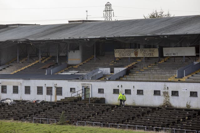 Two workmen in high-vis jackets walk within the seating area in Casement Park