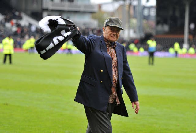 Mohamed Al Fayed waving a Fulham flag on a football pitch 