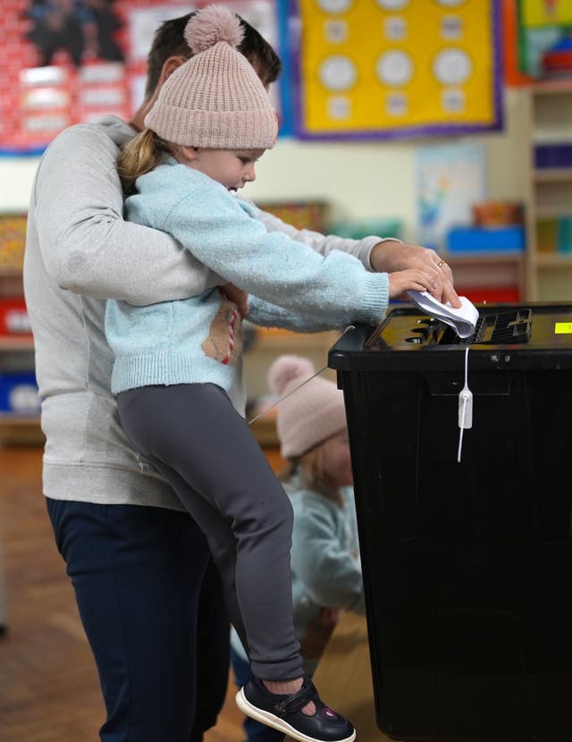 A woman lifts up a young girl so she can put a vote in a ballot box