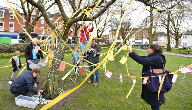 Ribbons, jokes, hand-made flowers and painted stones are added to a tree in Fortune Green (John Stillwell/PA)