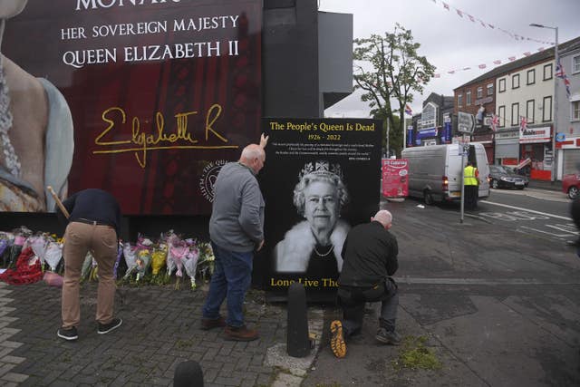 Council workers and local community representatives hang a mural on a wall in Crimea Street, off Shankill Road in Belfast following the Queen's death