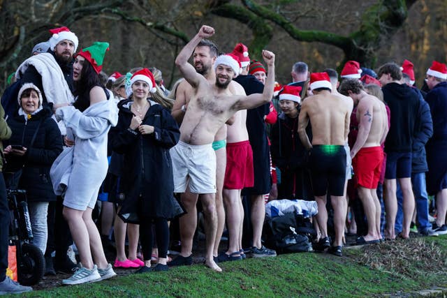 Swimmers, including one man flexing his biceps, prepare to take part before the Christmas Day dip in Blackroot Pool at Sutton Park
