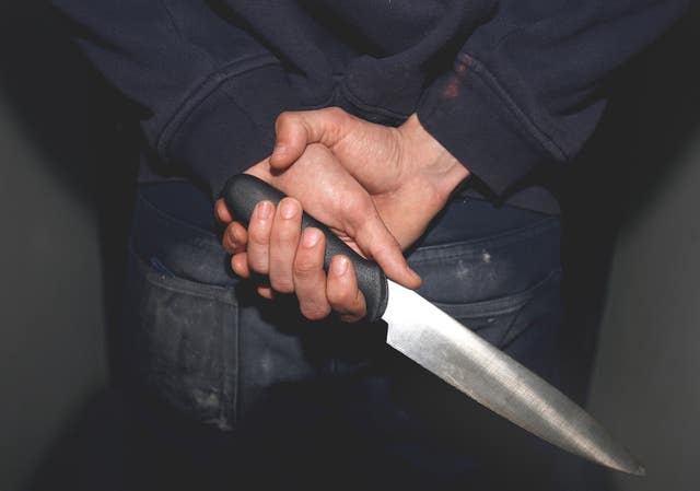 A general view of a man in a hoodie holding a knife