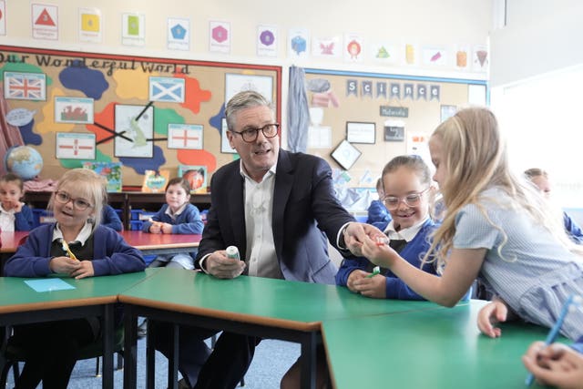 Sir Keir Starmer hands a school pupil a toothbrush and holds a toothpaste tube in a school classroom, ahead of a supervised teeth cleaning session