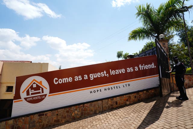 A security guard opens the entrance gate next to a sign reading ‘Come as a guest, leave as friend’