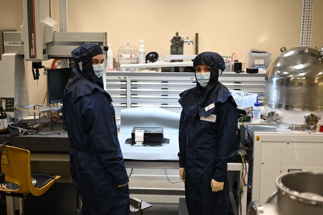 Two scientists in dark blue protective suits standing next to a component 