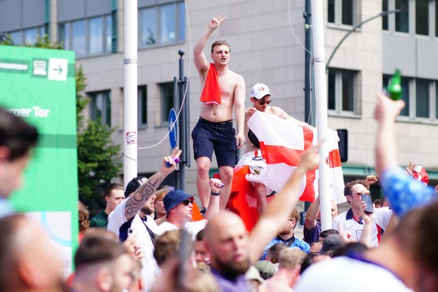 A shirtless man waves his arms and another man holds an England flag