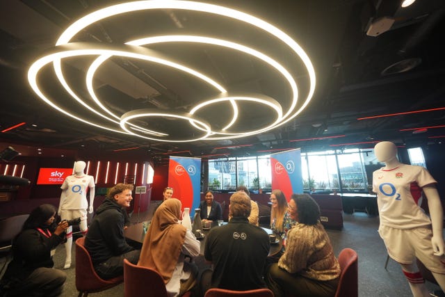 Kemi Badenoch talking to a group of students around a table. There's bright circular lights above and mannequins in rugby shirts dotted around.