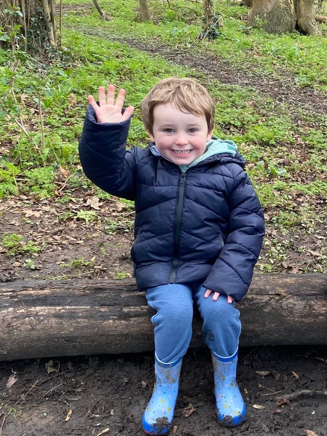 A little boy in a blue jacket waves his hand 