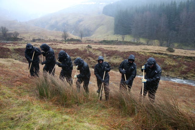 Police officers search undergrowth in a valley on the outskirts of Tyndrum