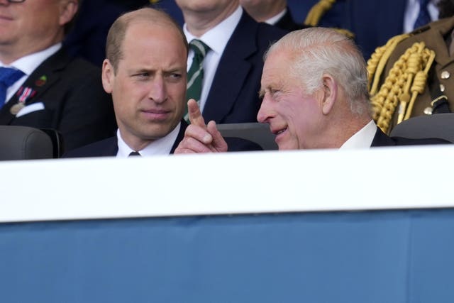 The King leans over to speak to son William as they sit together at the D-Day 80th anniversary commemorations