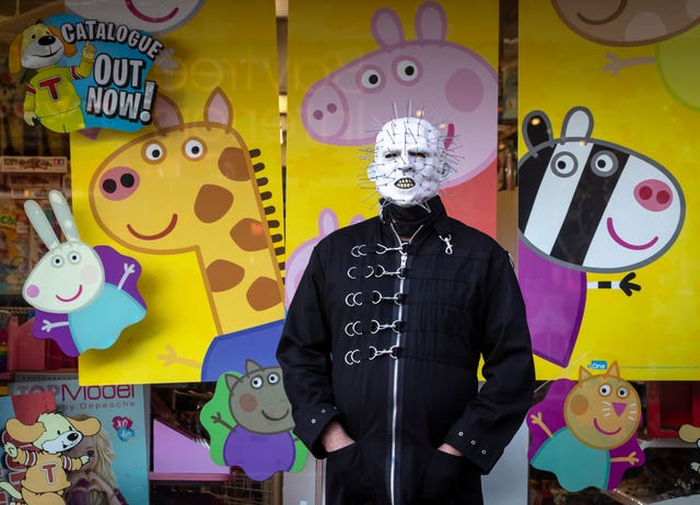 A goth poses for a photo in front of a shop window featuring Peppa Pig during the Whitby Goth Weekend in Whitby