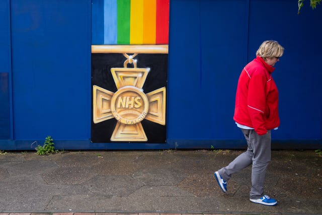 A woman passes a mural showing an NHS medal