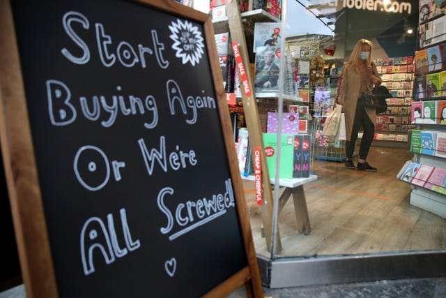 Notice on a billboard encouraging customers, while a person, wearing a face covering, browses inside a shop in Glasgow city centre, some six months on from the evening of March 23 when Prime Minister Boris Johnson announced nationwide restrictions