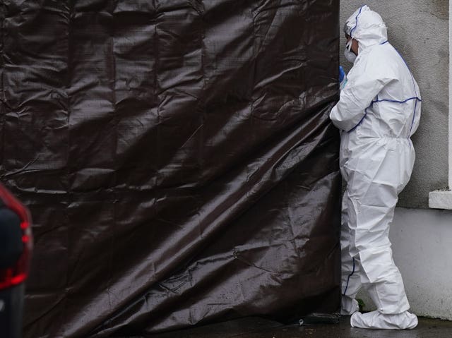 An officer in white forensics outfit next to black plastic covering a house