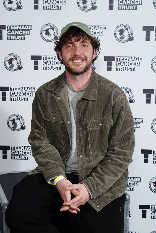 Seann Walsh smiling while posing for a photo in front of Teenage Cancer Trust signage