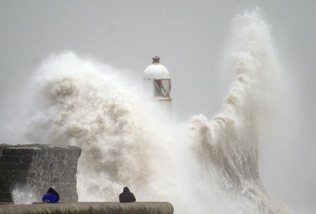 Waves crash over the seafront in Porthcawl, dwarfing the lighthouse as two people watch on