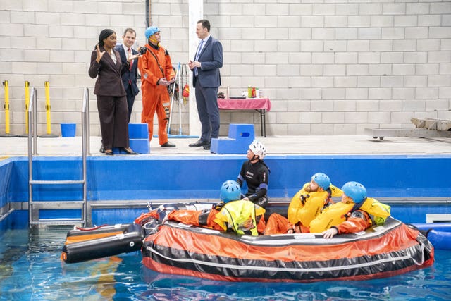 Kemi Badenoch, Russell Findlay and Andrew Bowie speaking at the side of a pool, with several people in a lifeboat in the water