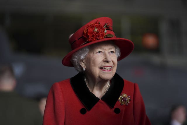 The Queen wearing a hat decorated with flowers smiles during a military visit