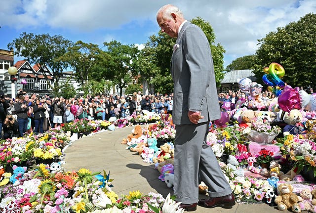 The King walking among hundreds of bunches of flowers and cuddly toys laid near the town hall