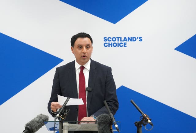 Anas Sarwar speaking from a lectern, with a large Scottish flag and the words 'Scotland's choice' behind him