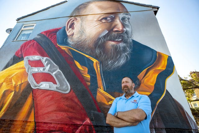 RNLI volunteer Mike Jones in front of a mural of him to honour of his 40 years of service