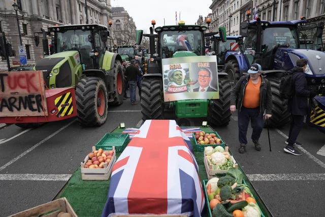 A coffin draped in the Union flag, surrounded by fruit and veg, with tractors behind it