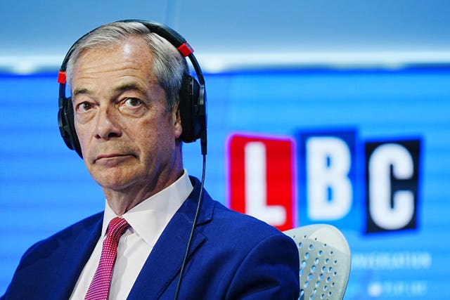 Nigel Farage sat in a chair wearing headphones with the LBC logo in the background