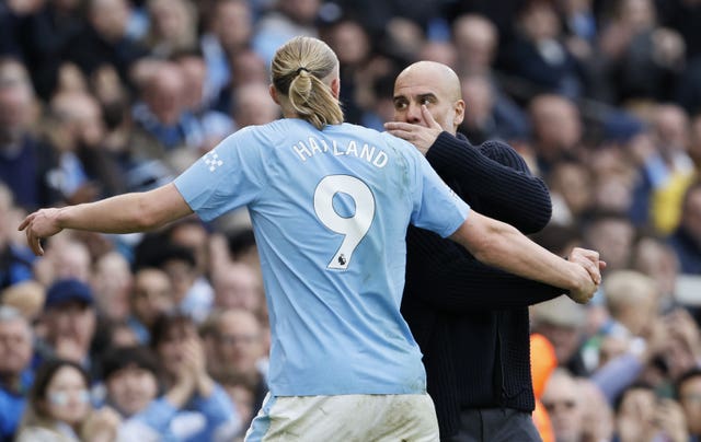 Pep Guardiola covers his mouth as he speaks to Erling Haaland