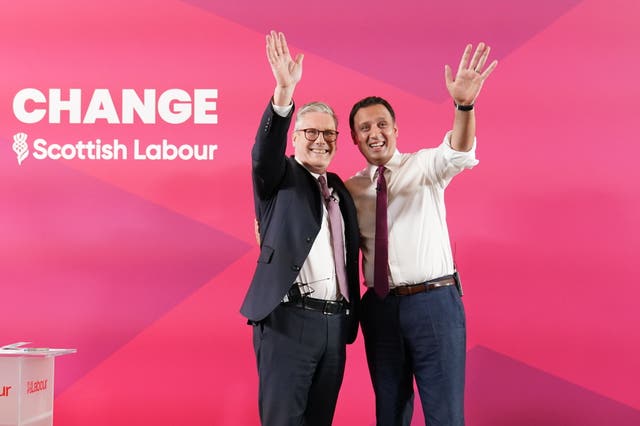 Sir Keir Starmer and Anas Sarwar smiling, each with one arm raised, in front of Labour signage