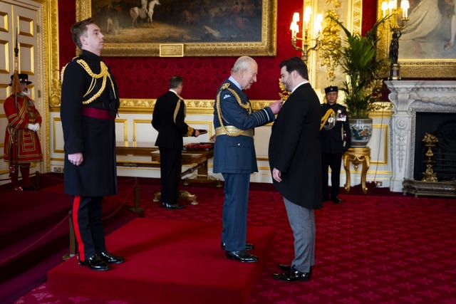 The King pins a medal on to the jacket of Richard O’Brien