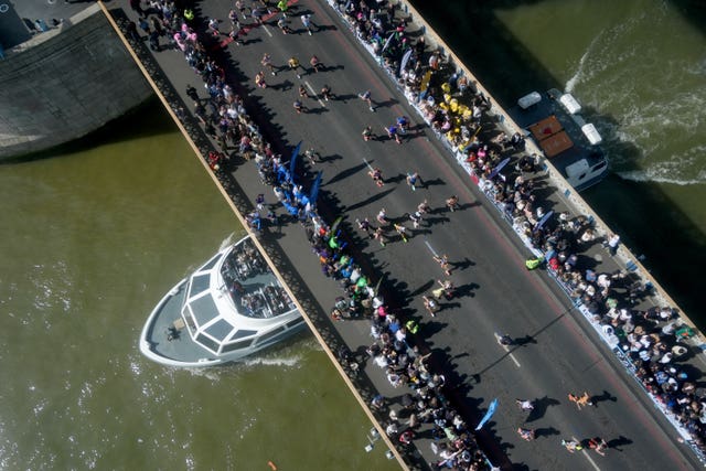 A boat passes under Tower Bridge, which is covered with spectators and runners 