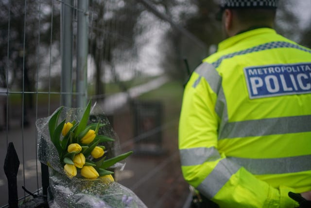 A policeman in a yellow coat looks at a bunch of flowers 