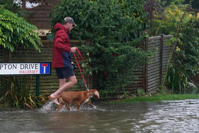 A man walking his dog on a flooded road in Frampton Drive, in Willersley village, Gloucestershire