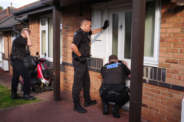 Three police officers at the door to a bungalow 