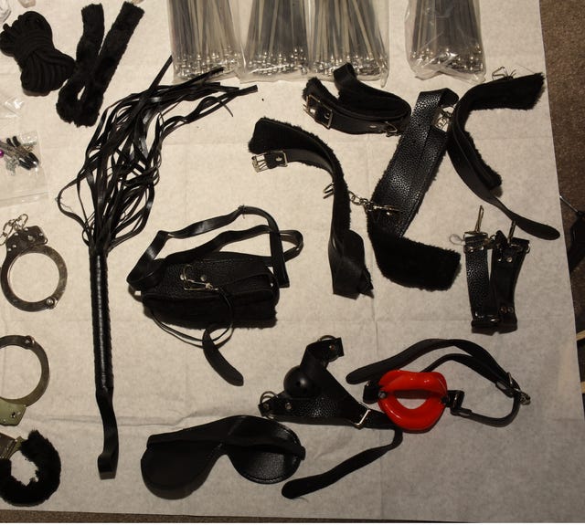 Items including handcuffs, cable ties and a whip on a white sheet
