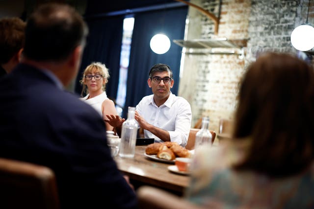 Rishi Sunak sits next to a woman at a table with food and bottles