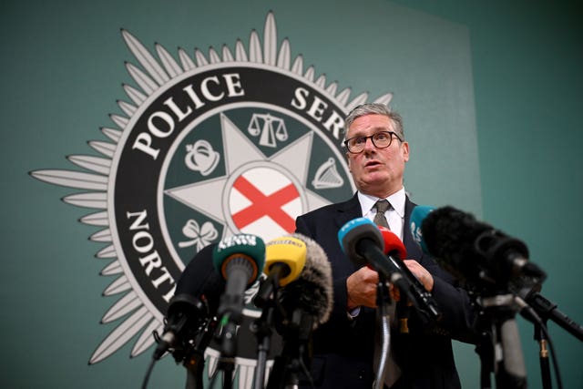 Keir Starmer speaking into microphones from the media while standing in front of a PSNI logo