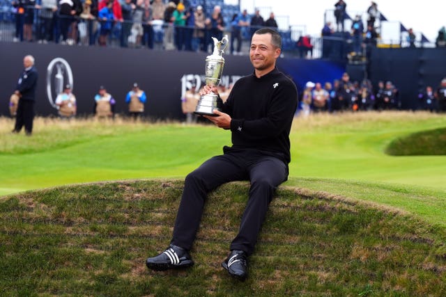 Xander Schauffele sits on the edge of a bunker holding the Claret Jug