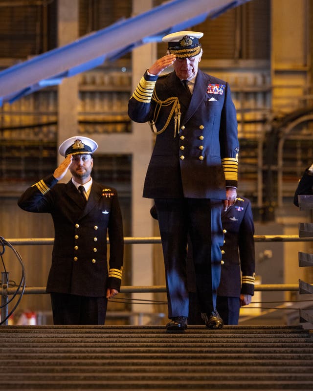 The King and senior submariners salute during his visit to a naval base