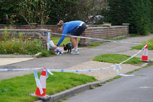 A woman leaving a floral tribute outside a property in Hammond Road, Woking