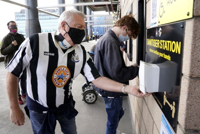 Face mask-wearing Newcastle fans use a hand sanitising station ahead of the Premier League match against Sheffield United at St James' Park. Despite the season ending on the high of having supporters back in stadia, the experience of attending matches is noticeably different to pre-pandemic conditions. Football fans will have to adapt to a 'new normal' at grounds, with the wait for the return of capacity crowds set to continue for the foreseeable future (Owen Humphreys/PA)