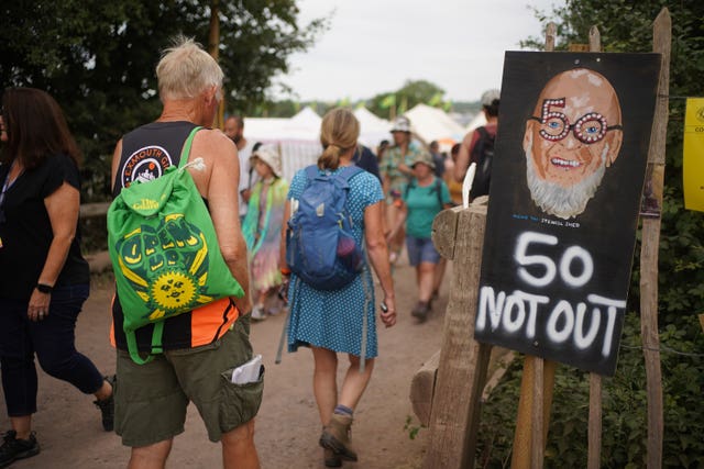 Festival-goers walk past a Michael Eavis sign