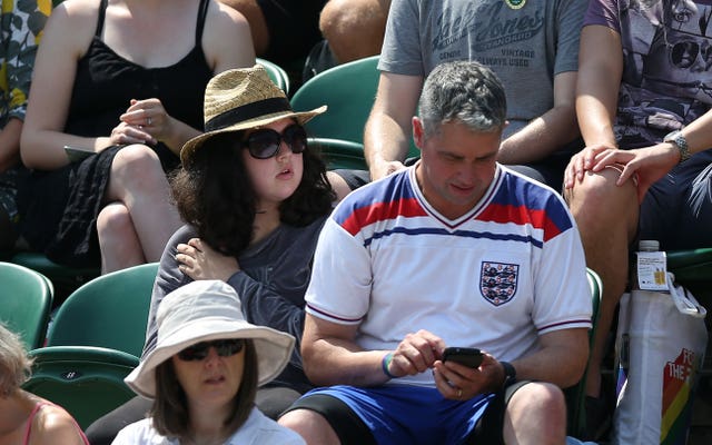 A man wearing an England shirt watches the World Cup on his phone at Wimbledon