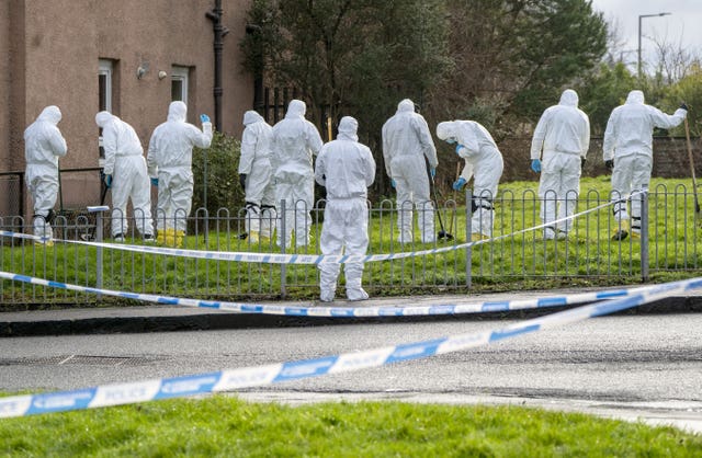 A number of police forensic officers in white suits searching an area of grass